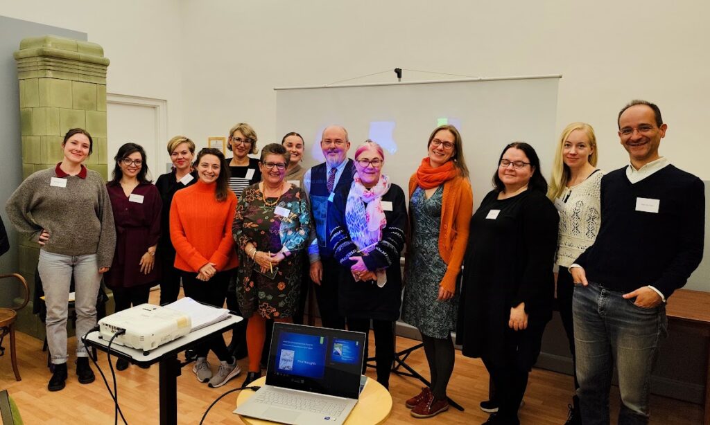 The Workshop Group at the first European Biblio/Poetry Therapy Conference, with Geraldine Campbell and David Madden. A group of people wearing colourful clothes stand in a line and are smiling at the camera.